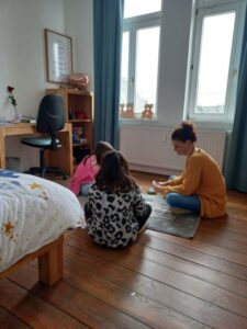Erzieherin und zwei Kinder sitzen auf dem Boden in einem Kinderzimmer und spielen Karten